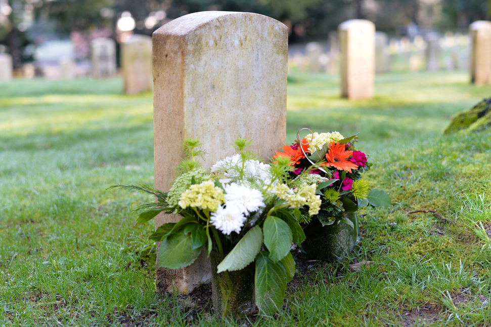 A weathered headstone with fresh flowers laid at its base